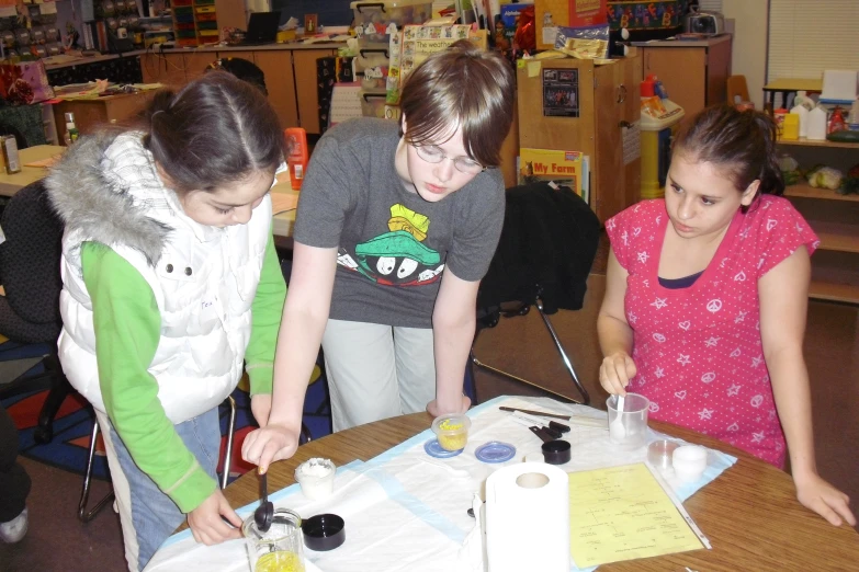 three girls look at a table with a ruler on it