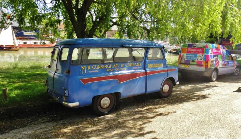 an old, bright blue van parked on the side of a road near a pond