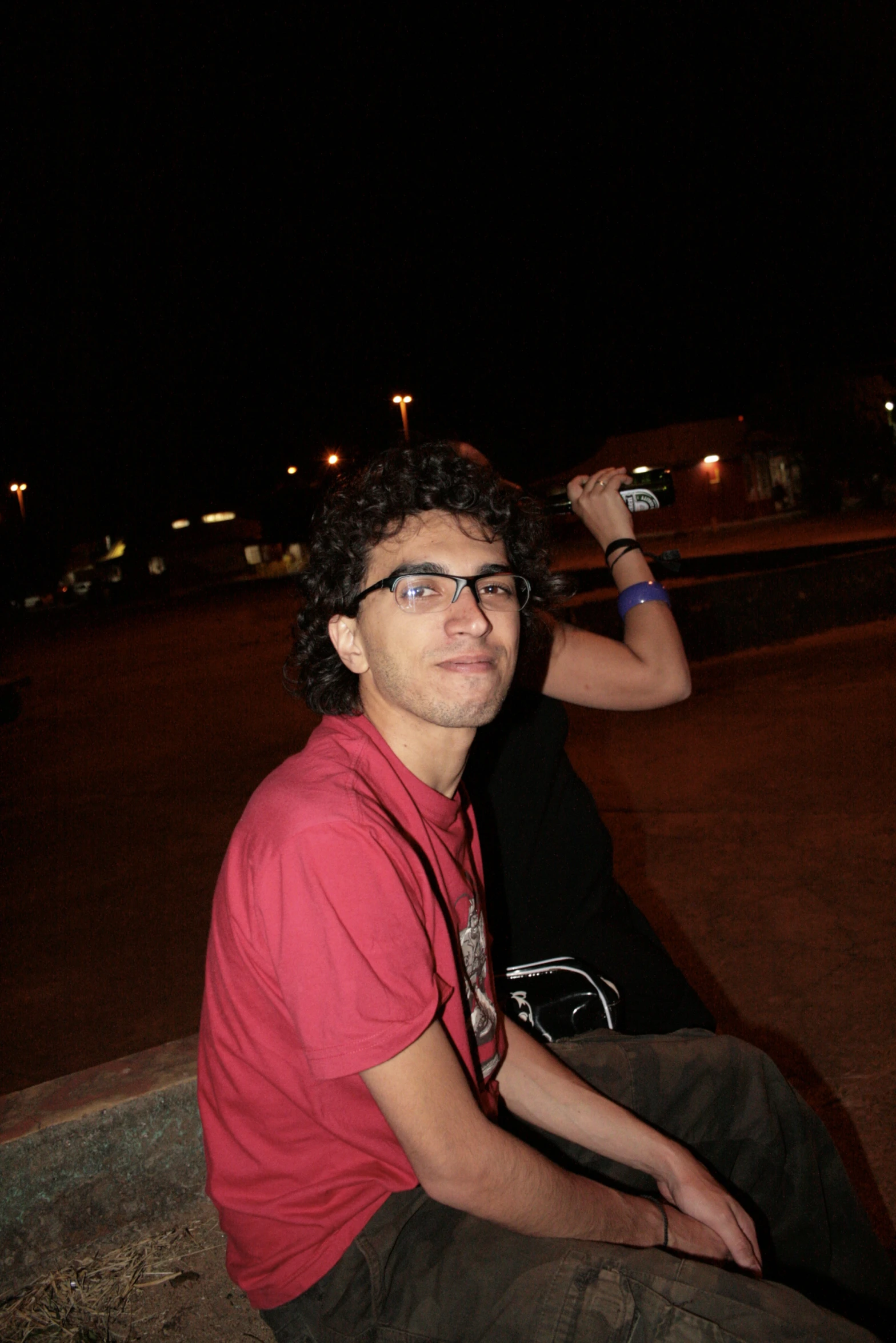 a man sits on the ground at night while holding a cell phone in his hand