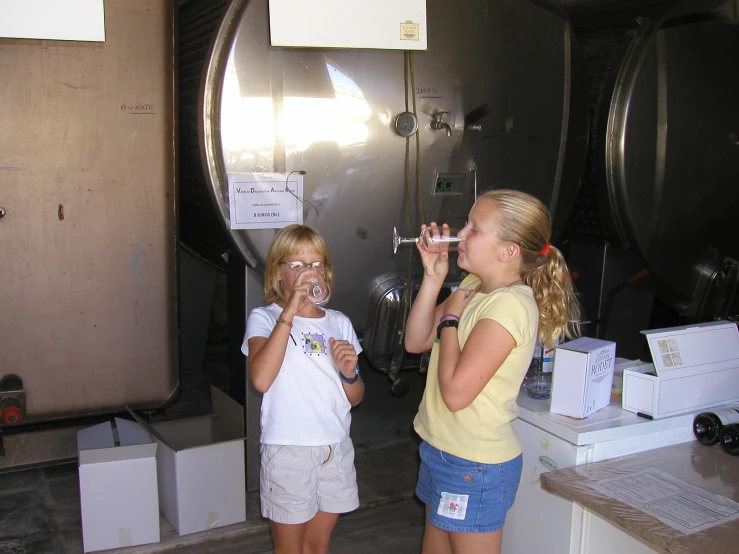two girls drinking beverages standing by a wine storage