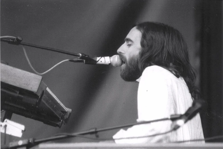 a man standing at a microphone with a piano and keyboard