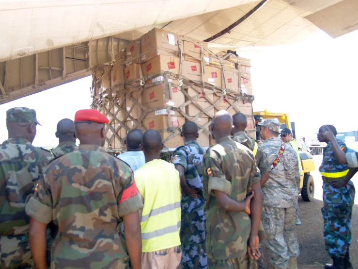 soldiers in camouflage look at an airplane loading boxes