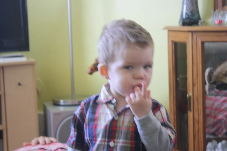 a little boy that is standing up with his hand near his mouth