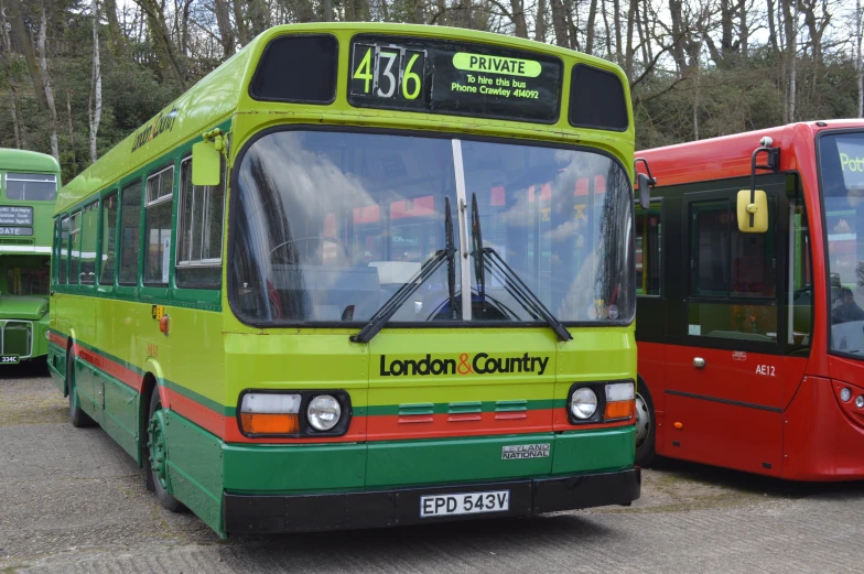 a green and red bus in front of other buses