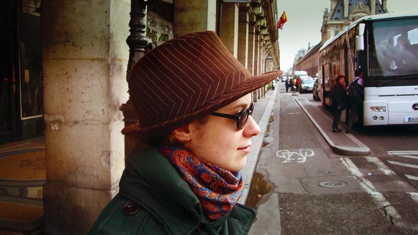 the woman wearing a hat stands near a bus