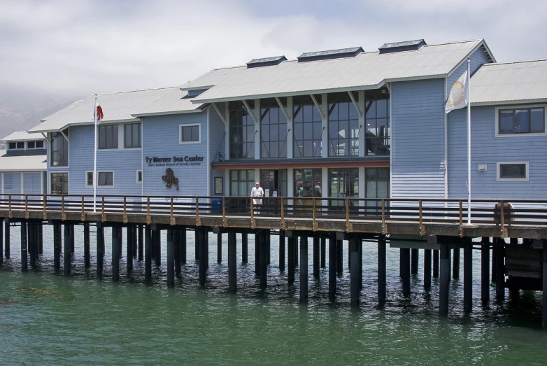 a long wooden dock next to some blue buildings