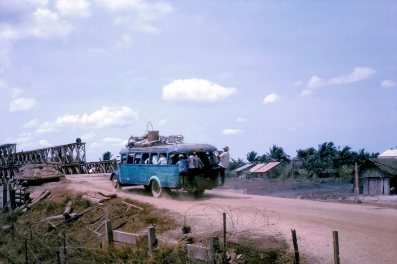 a old bus traveling across a bridge on a dusty road