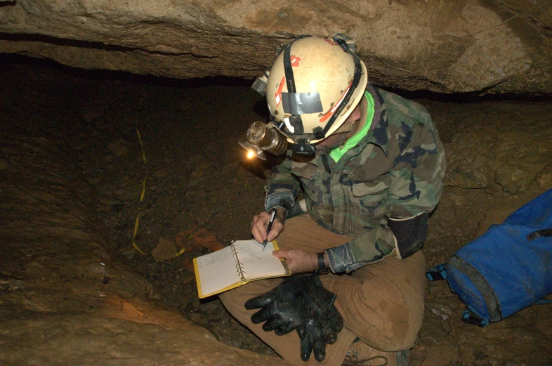 man in camouflage is holding a book inside of a cave