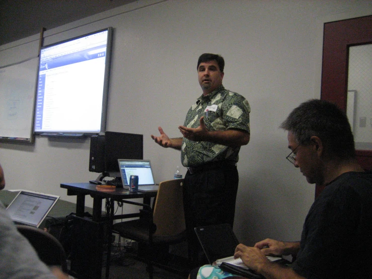 a man stands in front of a screen while gesturing to another person