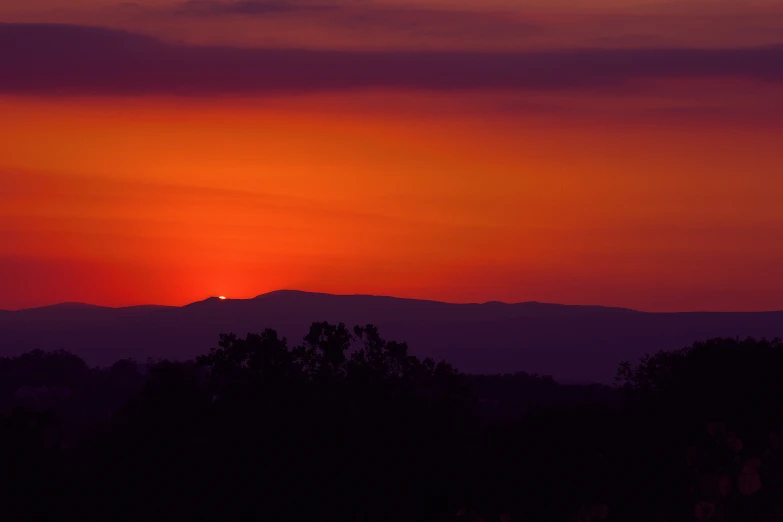 a sunset is seen behind some trees and hills