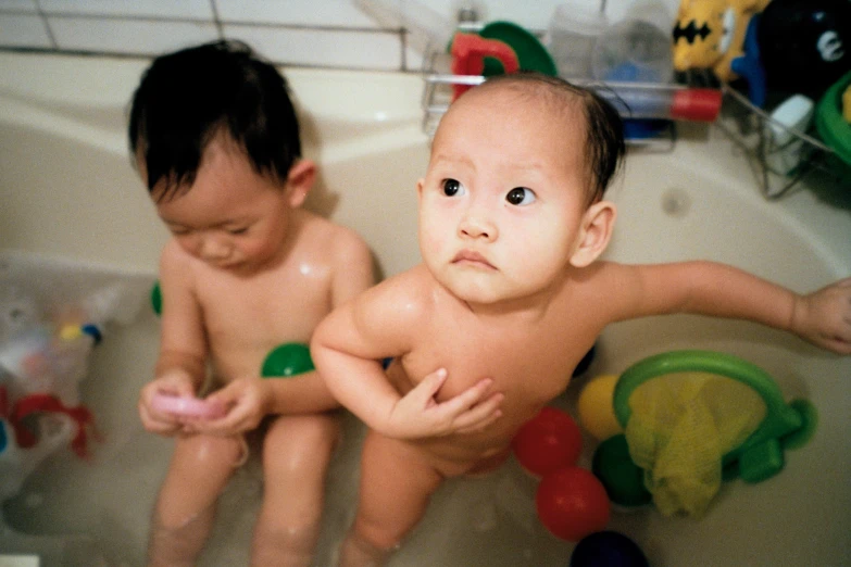 two babies in a bath tub with toys on the floor