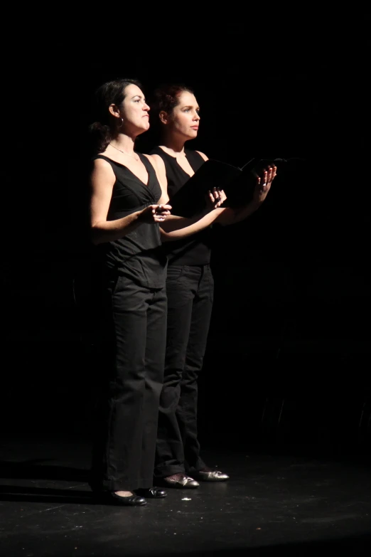 two women on stage are holding items in the dark