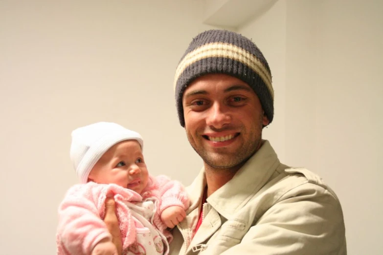 a man holding up a small baby with a knitted hat