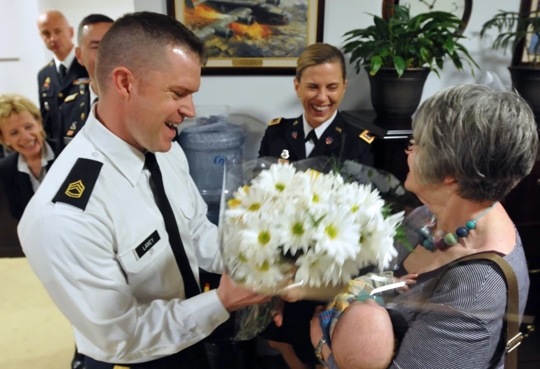 a woman is talking to a man in uniform and holding a bouquet of daisies