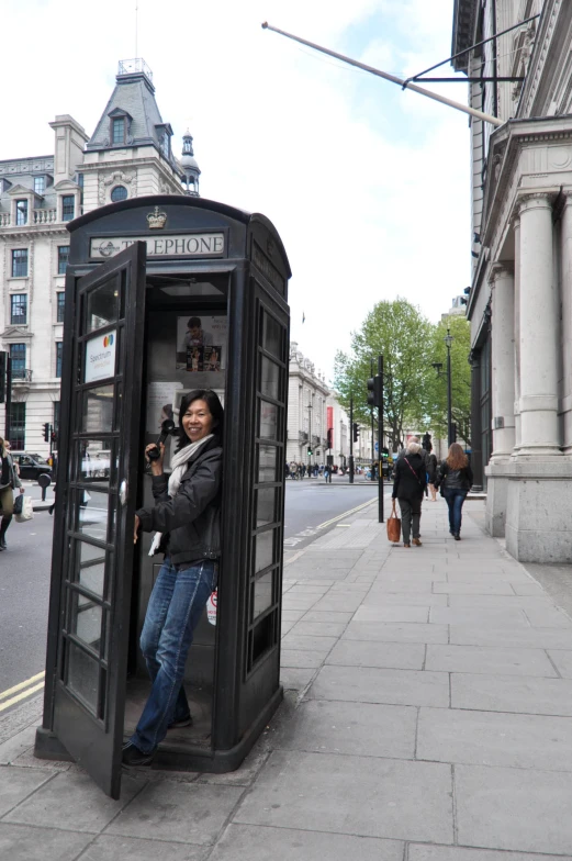 man taking a picture out of a public phone booth on a sidewalk