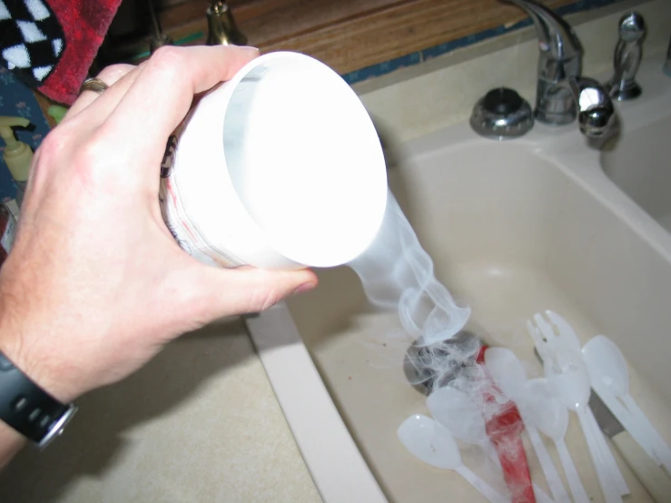 a person's hand holding a white container that is in a sink