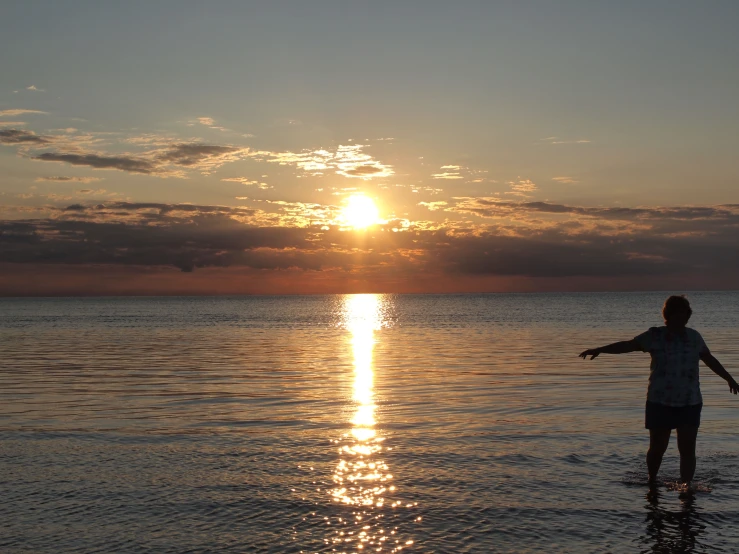 a young man standing in the ocean at sunset