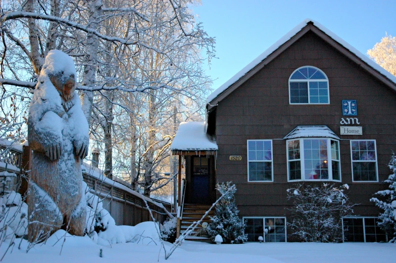 a house is covered in snow in front of a snowy forest