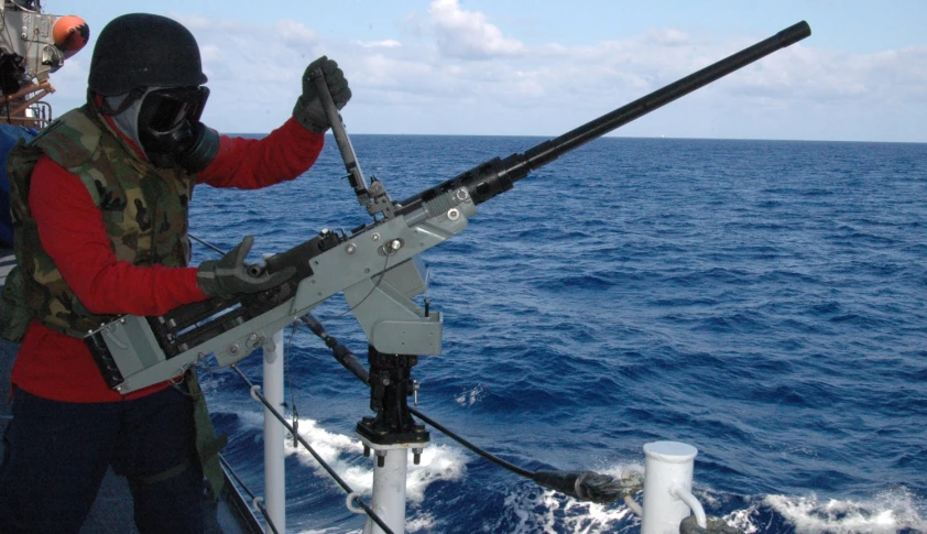 a man holding up a large rifle next to a ship in the ocean