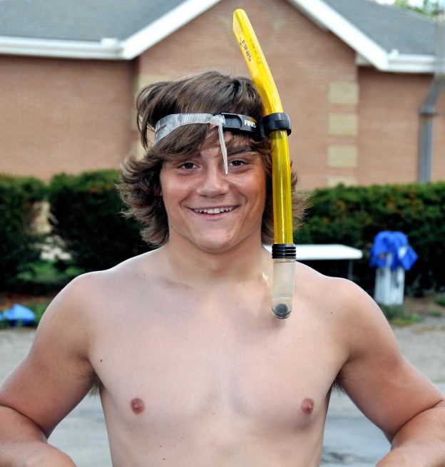 a shirtless young man holding a goggles and water hose