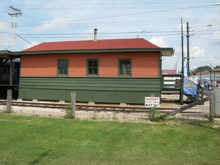 an orange and green house with a red roof sitting on some railroad tracks