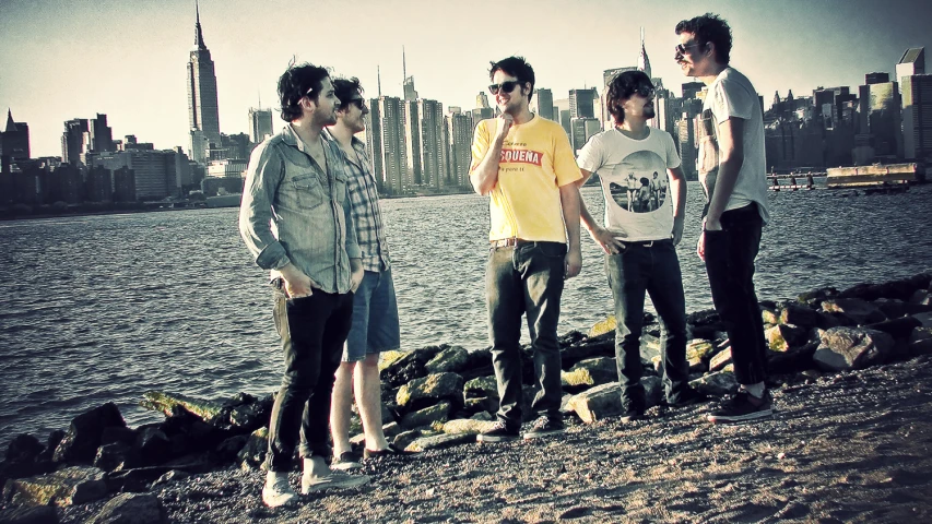 five men stand on rocks near the water and look out over city