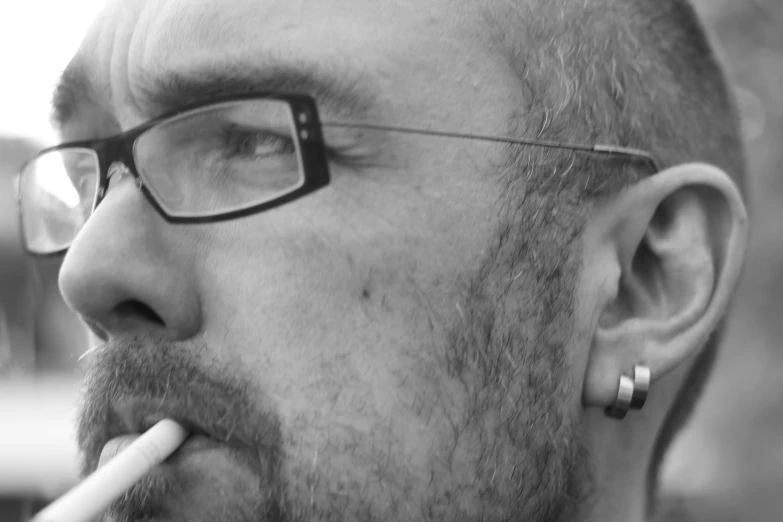 black and white po of man with thick rimmed glasses, piercings and cigarette