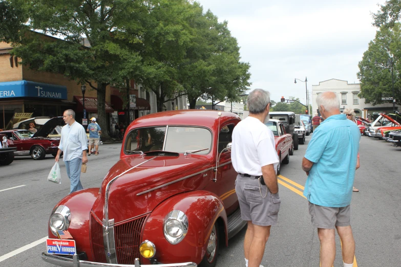 two men standing on the side of the road by a car