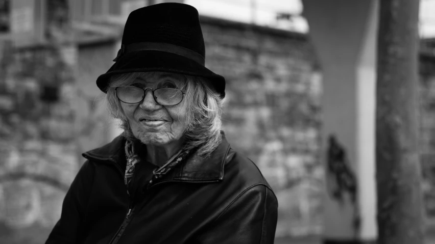 a black and white po of an older man wearing glasses, a hat and a leather jacket