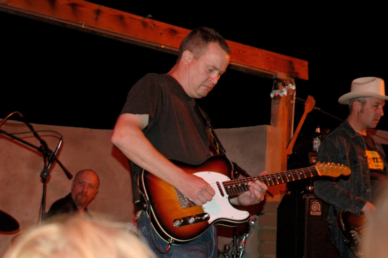 the man is playing his guitar with other people watching