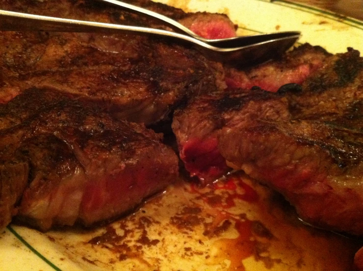 two steaks on a plate with a fork and serving utensils