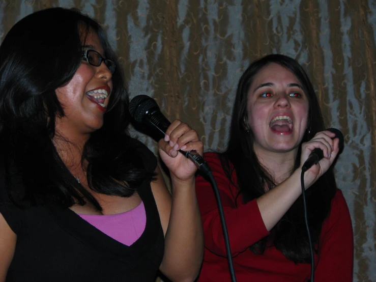 two woman standing up singing into microphones together