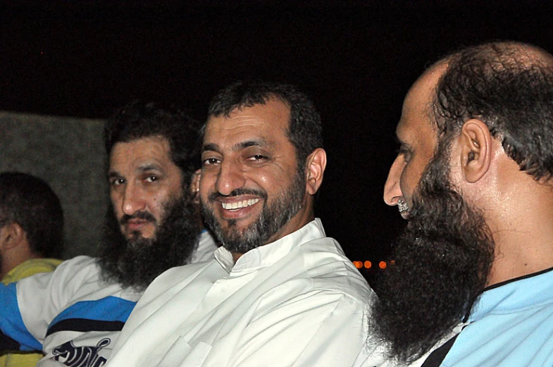 a man wearing a white shirt standing next to two others