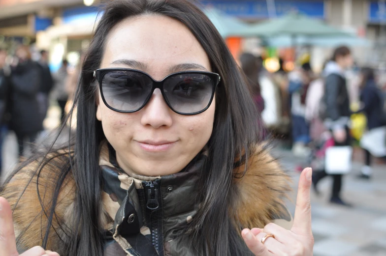 a woman with long hair and dark glasses stands in a busy street with her hand written peace