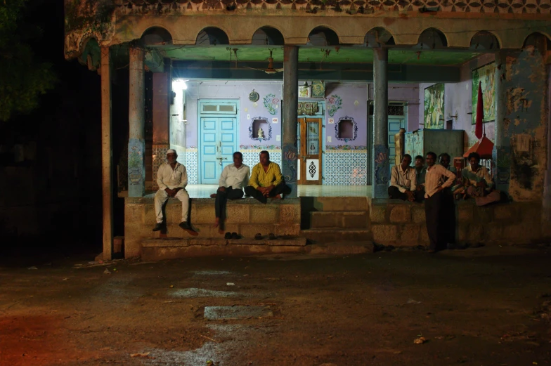 a group of men siting at the porch in front of a building