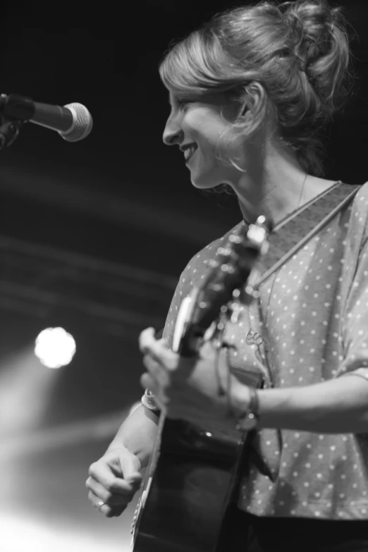 a woman is playing a guitar in front of a microphone