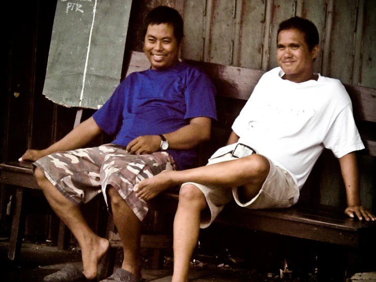 two young men sitting on a bench next to each other