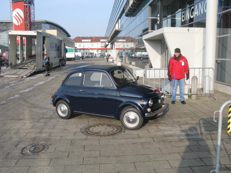 man talking on a phone beside his car in front of a train station