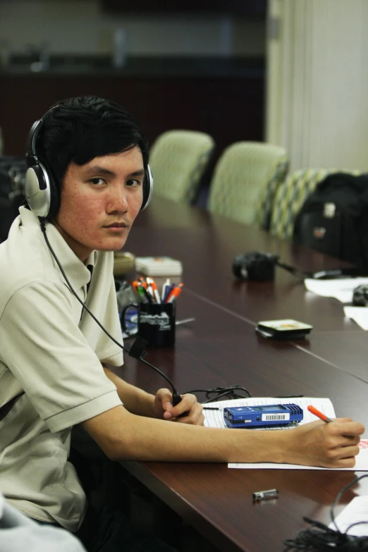 the young man is sitting down at the desk and listening to headphones