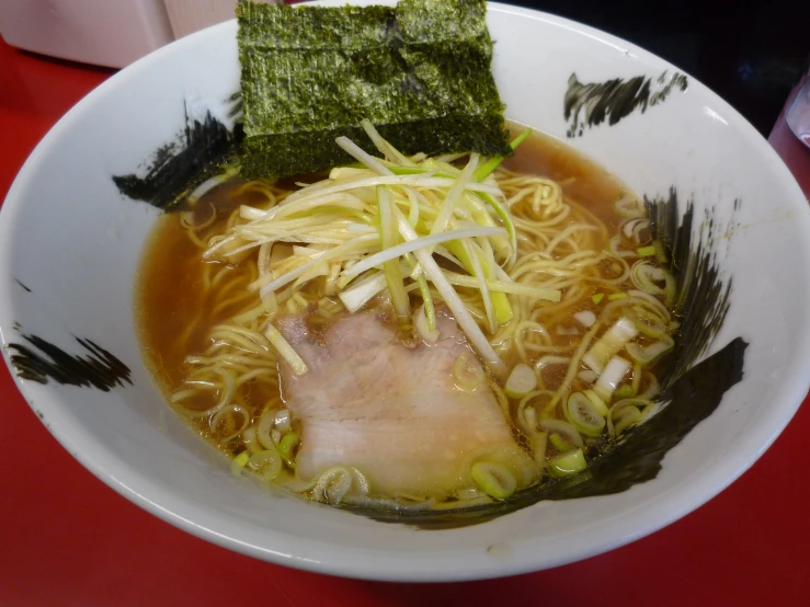 a bowl of noodles and meat and vegetable on a red table