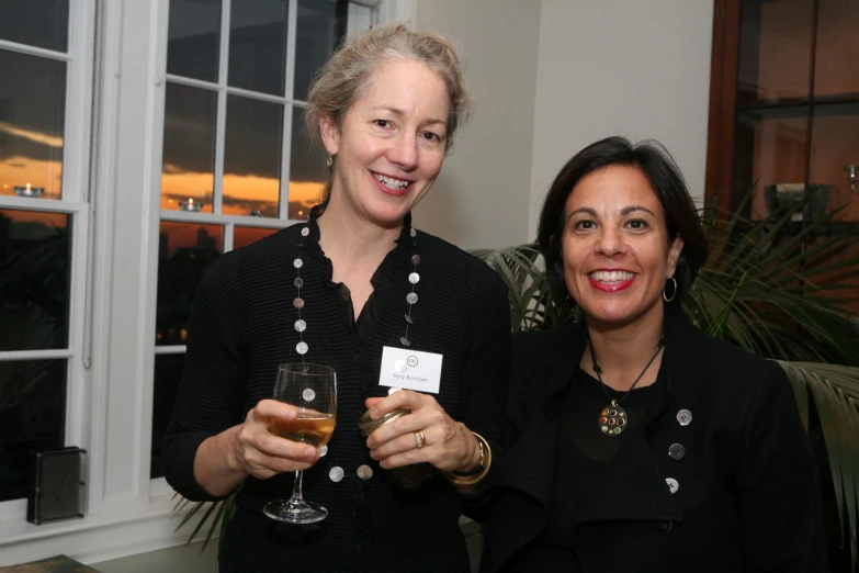 two women stand smiling, holding wine glasses