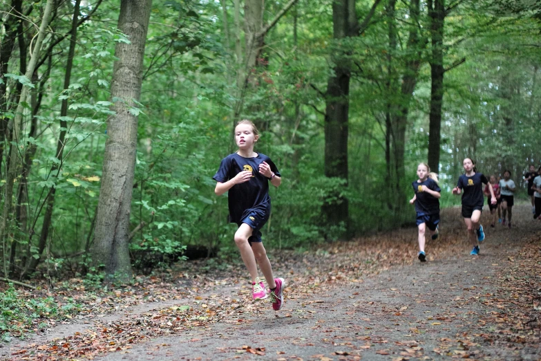 children run down a forest trail in front of a group of trees