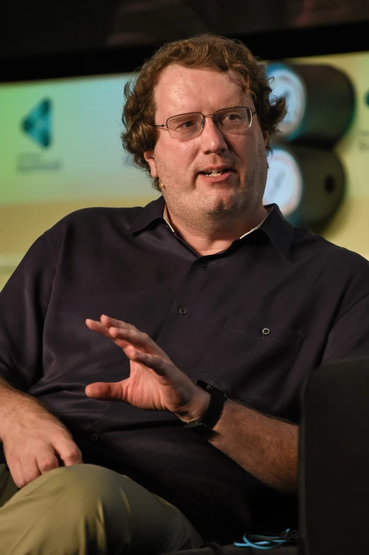 a man in glasses sitting down while talking to someone