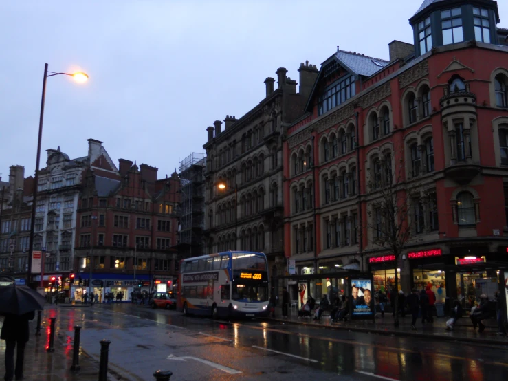 a busy street with pedestrians, busses, buildings and people standing around