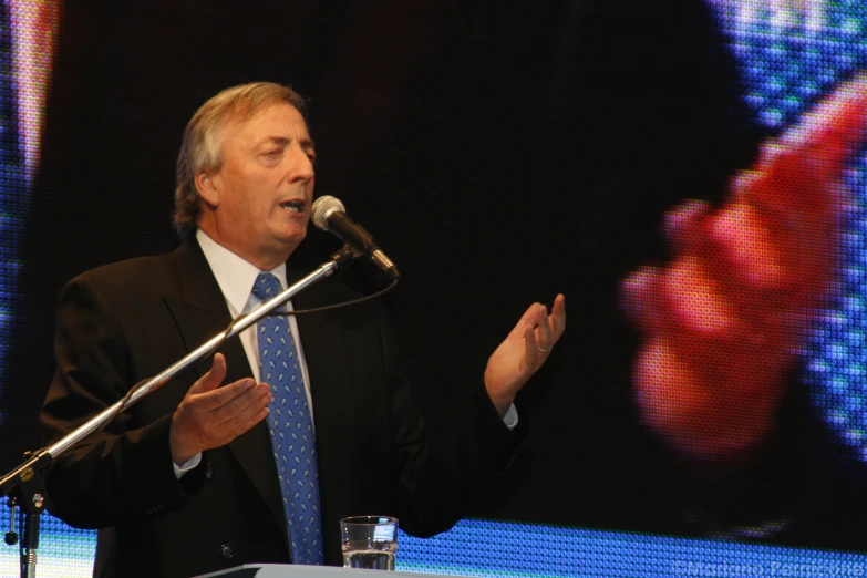 an older man holding his hands out for a speech