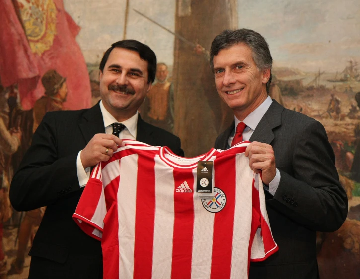 two men holding up a soccer jersey in front of a painting