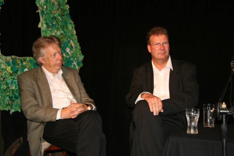 two men sitting on stage talking during a political event