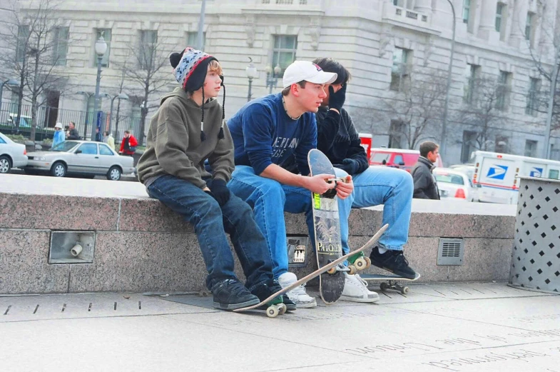 two boys sitting on a cement wall and one boy with a skateboard