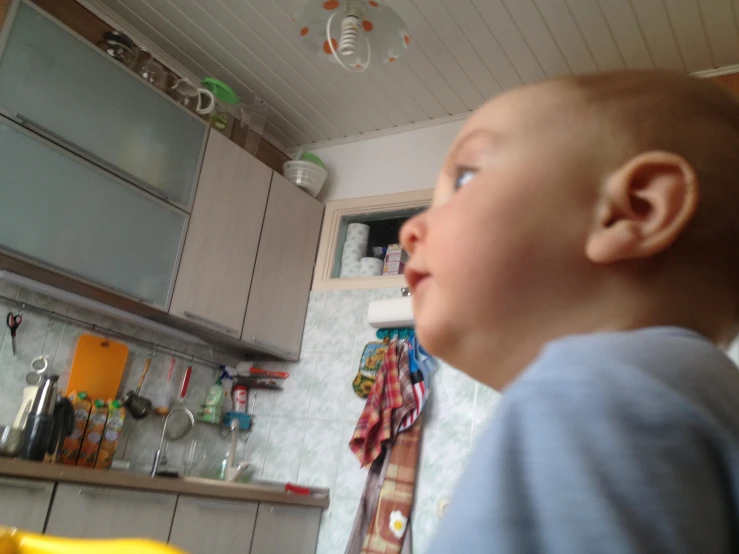 a baby in a kitchen staring back at soing off in the distance