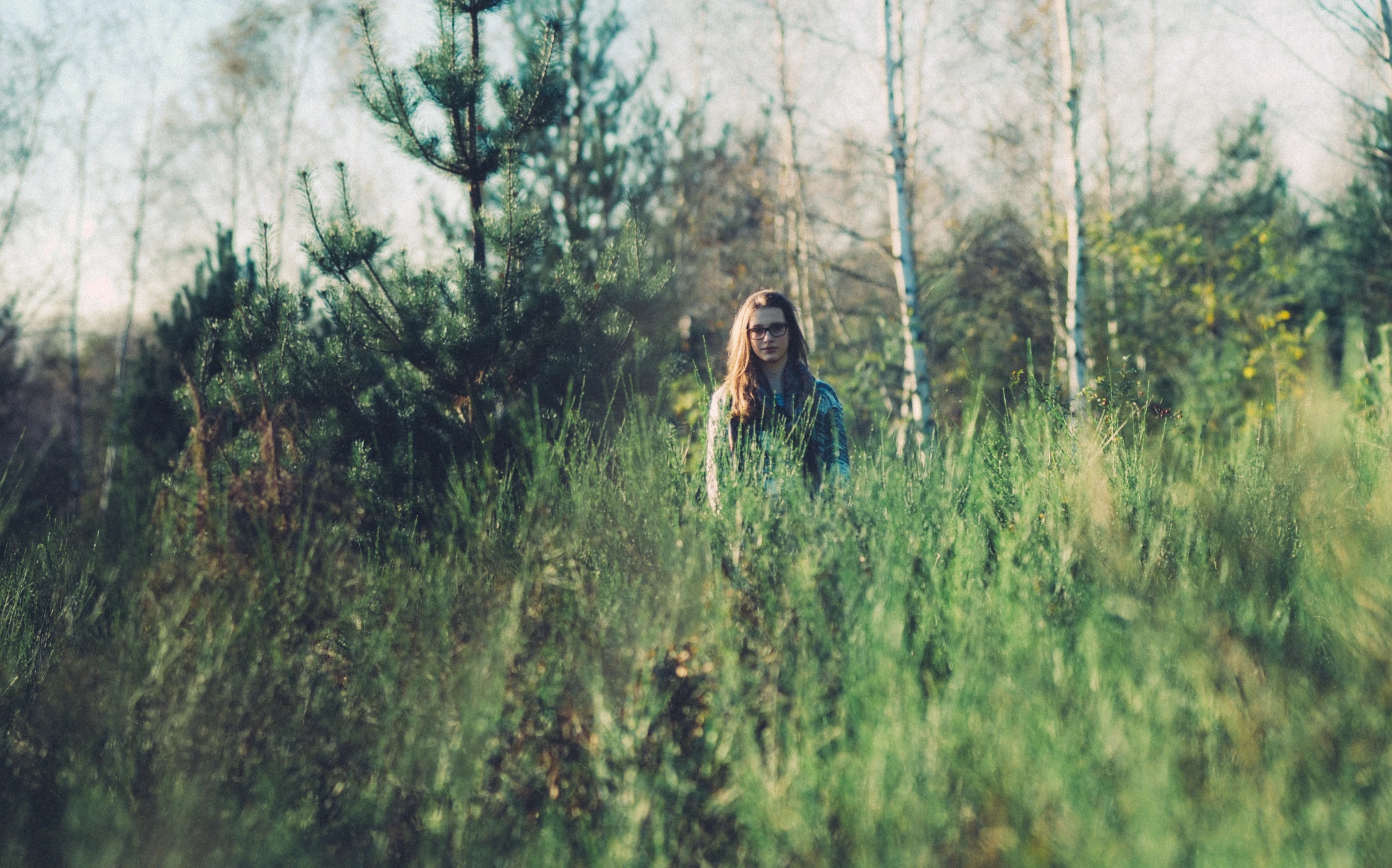 a girl in blue shirt standing among trees and bushes
